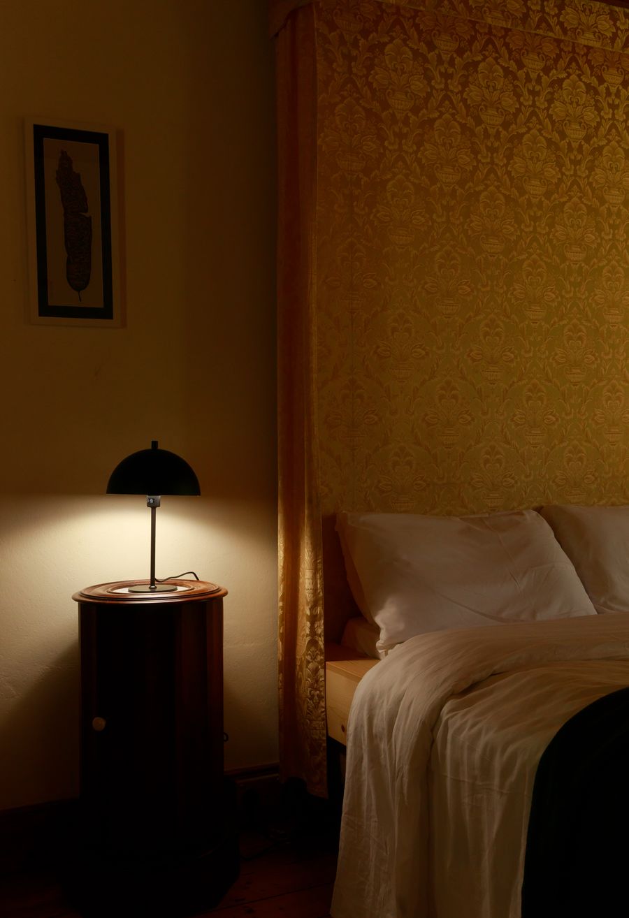 A lamplit bedroom at the Garden Retreat, gold damask walls above turned-down linen