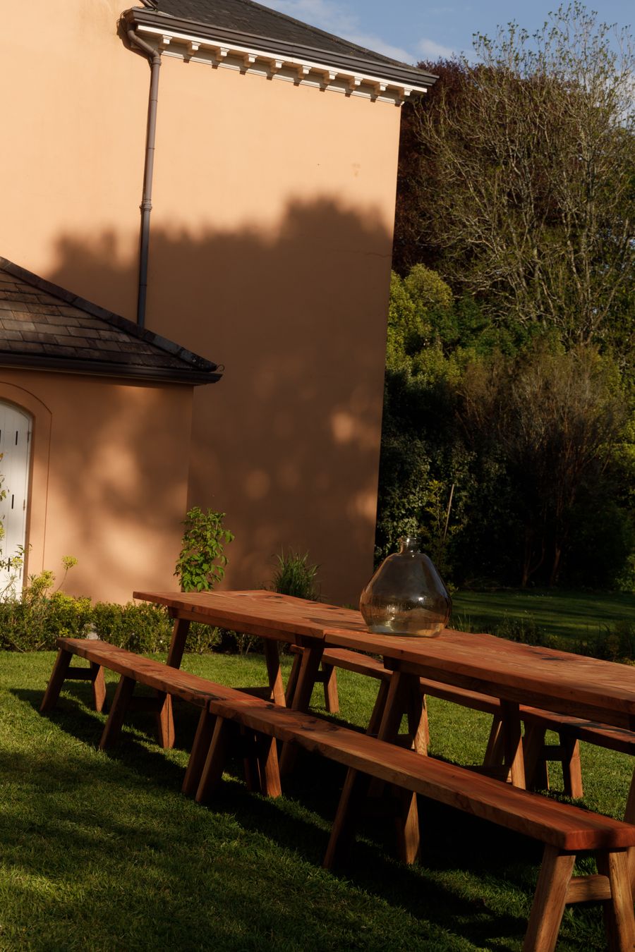 Long trestle tables and benches set out on the lawn beside the terracotta-washed house